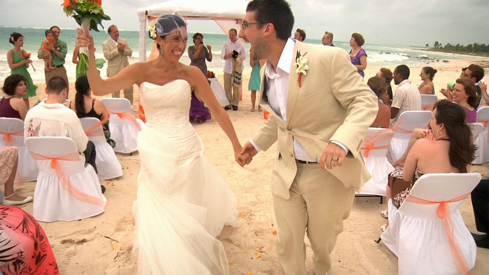 A bride and groom walk down the aisle, celebrating, on a beach