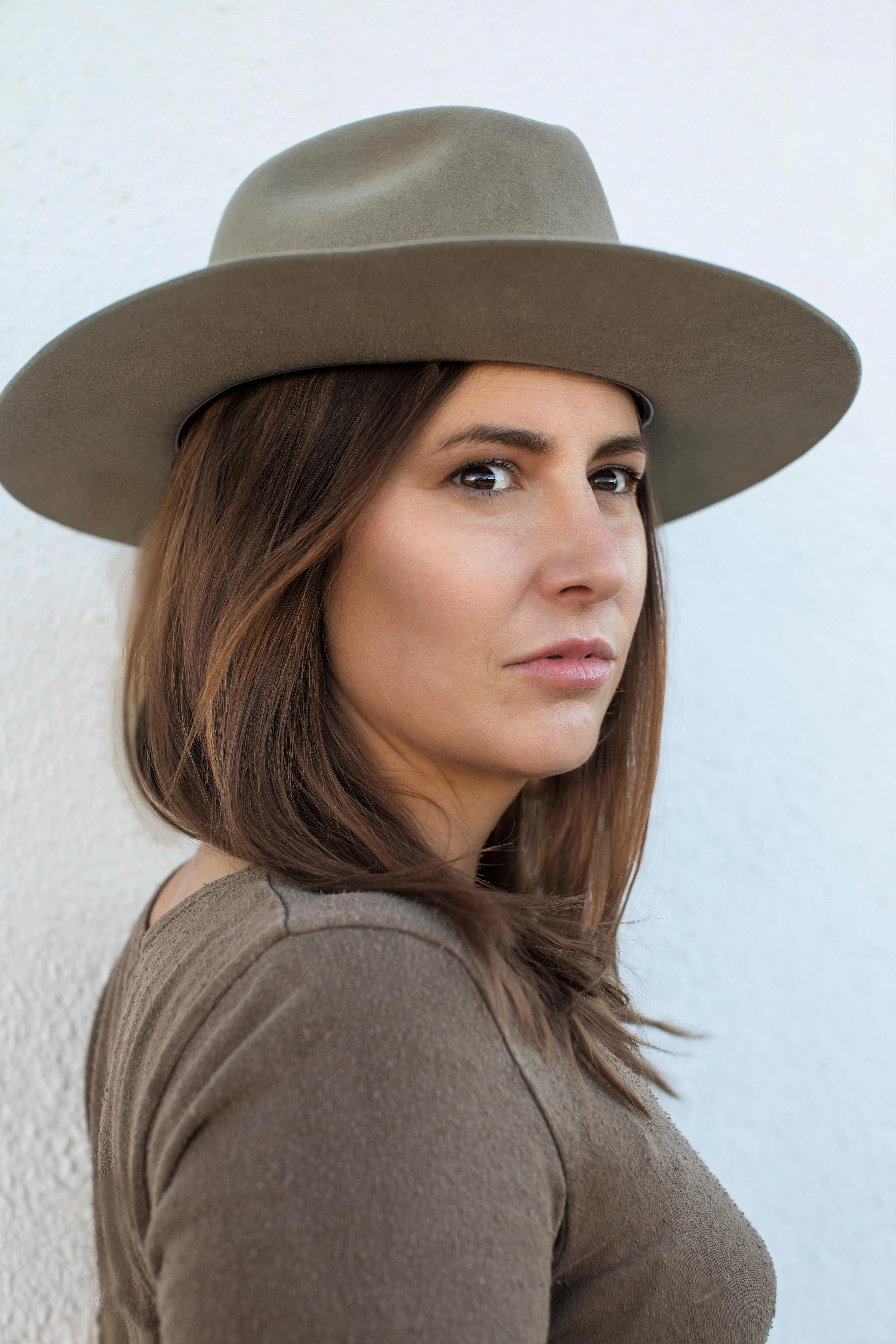 Woman with straight brown hair wearing a brown shirt and brown hat, looking off to her right in the distance
