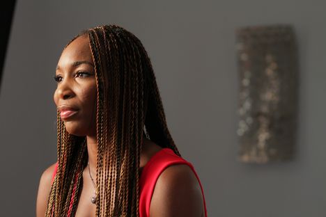 Venus Williams, a middle-aged black woman with long black braids, sits looking at someone in the distance, wearing a red sleeveless dress