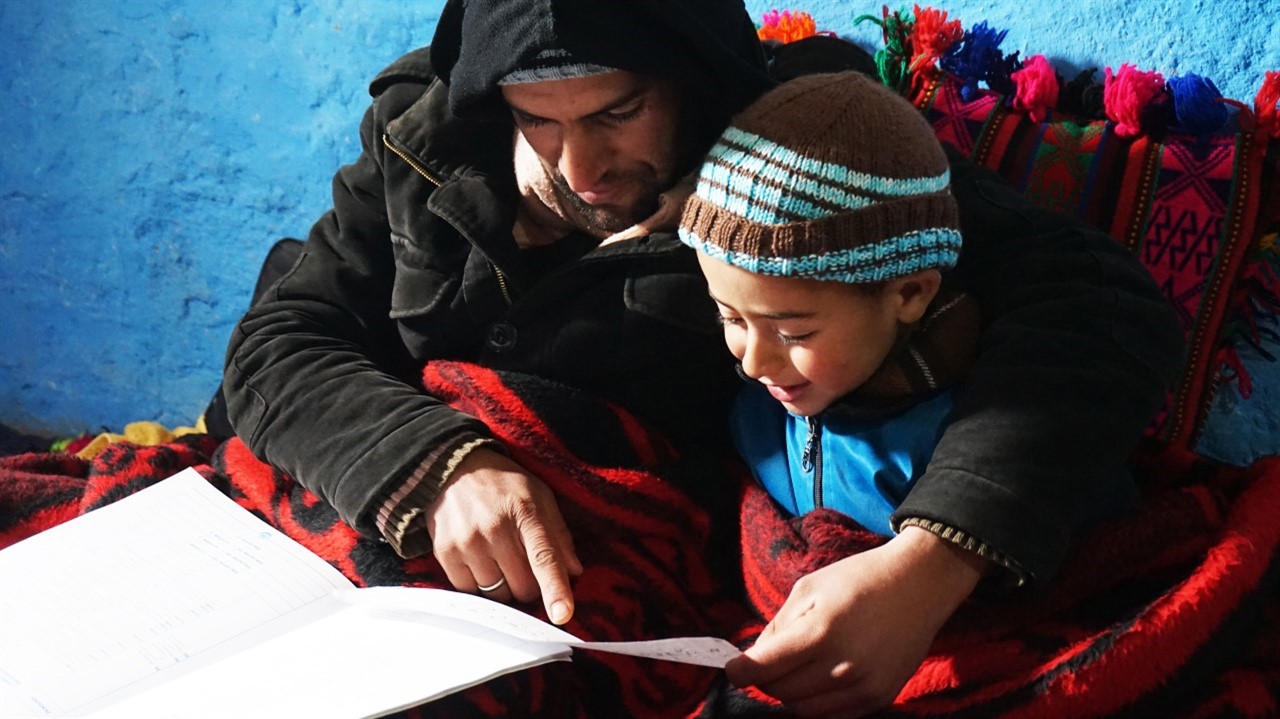 An Indigenous Moroccan helps his child with his school lesson. Both are wearing warm winter clothing. From Mohamed El Boudi’s 'School of Hope', courtesy of Hot Docs.