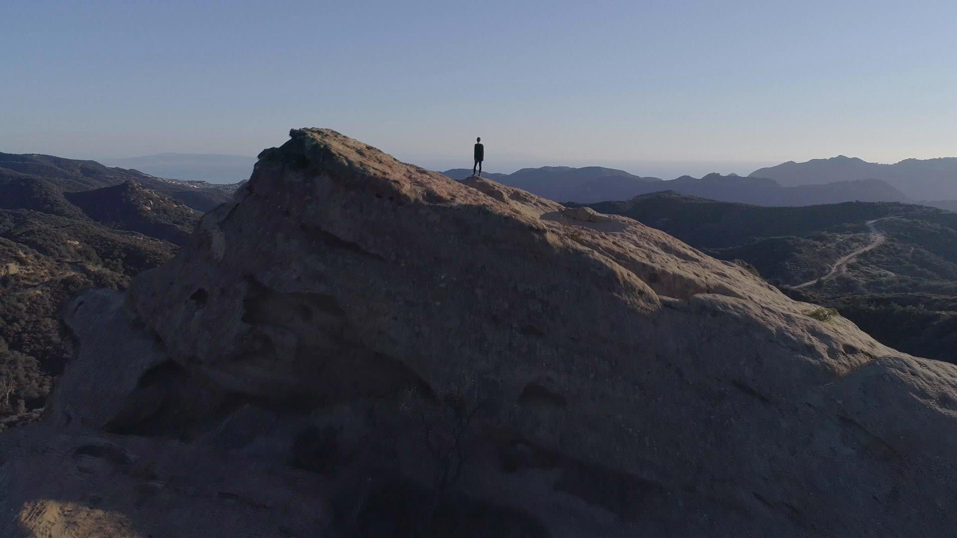 Blue skies and mountains with a person standing alone on one mountain.