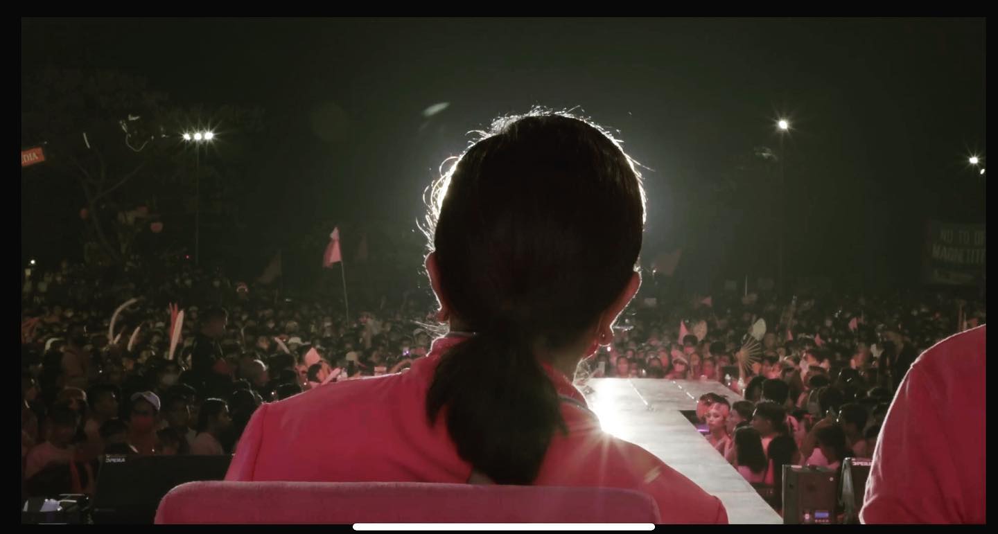 A woman wearing a pink top with black hair shot from the back. She is front-lit.