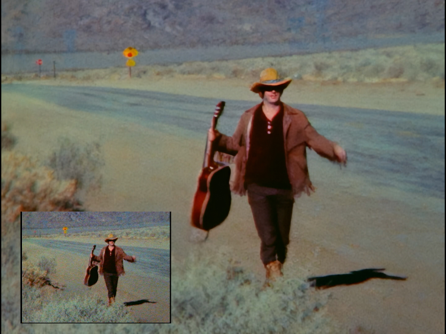 An image is shown twice, once in the bottom left hand corner of the frame and once taking up the frame's entirety. They both picture a man in a cowboy hat with a guitar on a desert road. The larger sized image has been digitally restored, and looks much smoother and cleaner. 