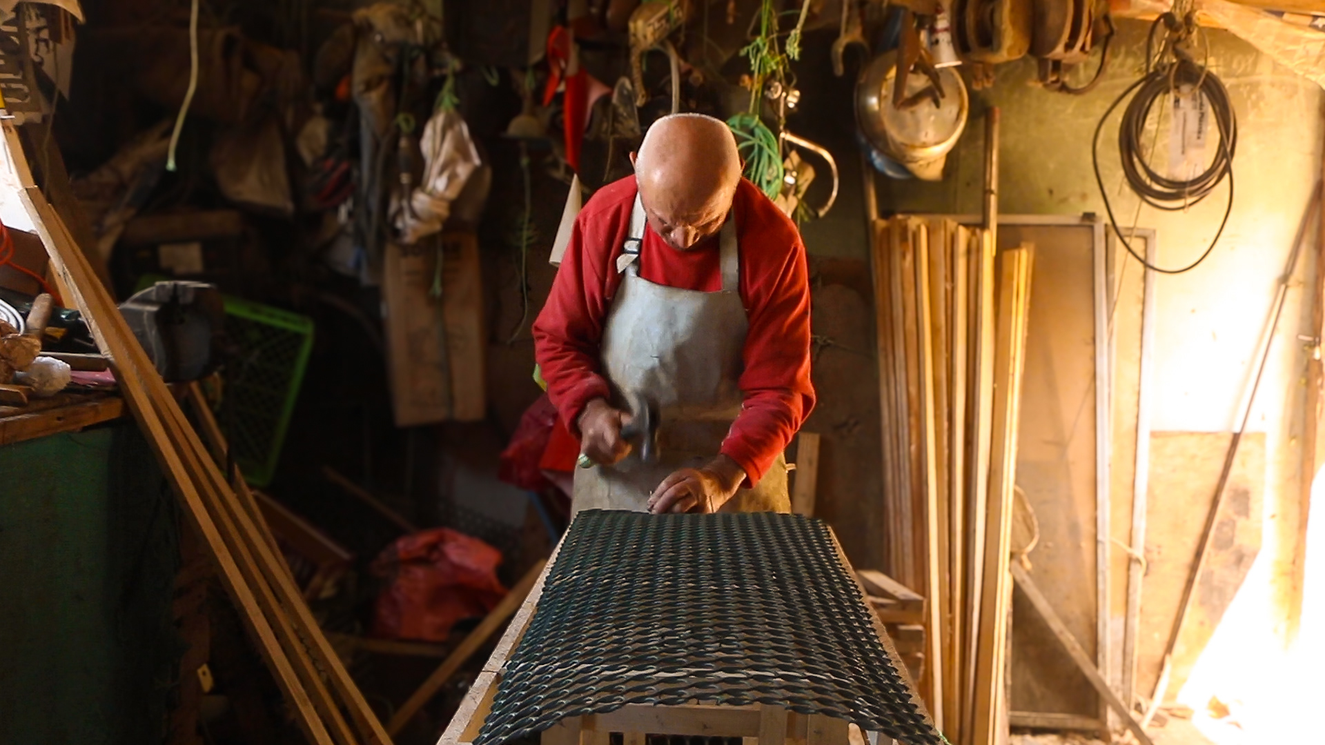 A man in a red shirt beds over a worktable.