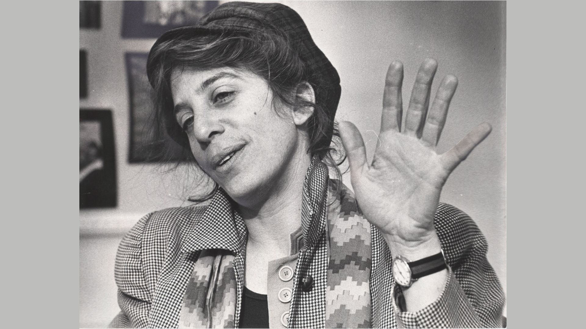 Black and white photo of a white woman with dark hair pulled back under a hat, wearing a scarf and a coat