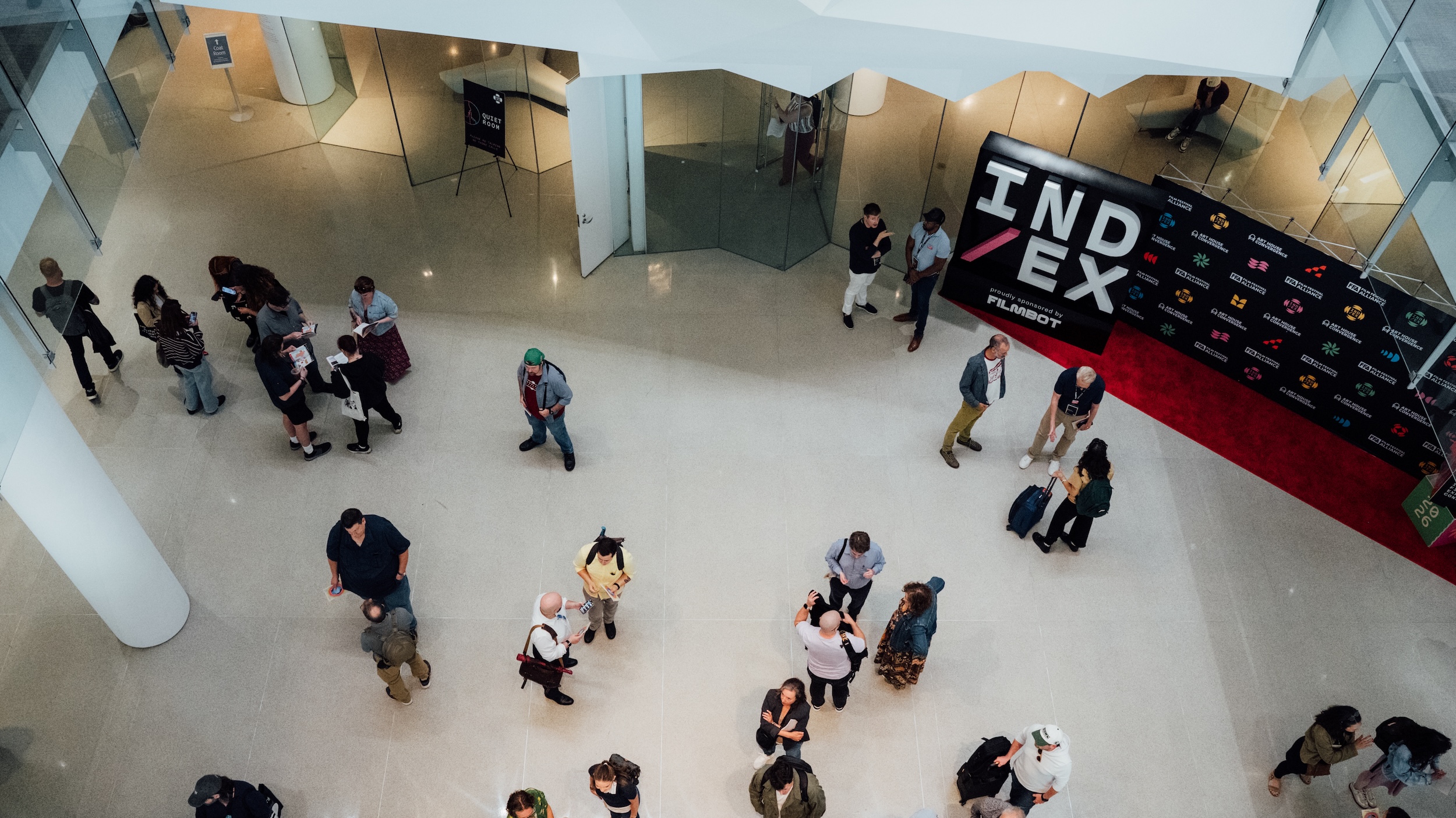 Bird's eye view of a gathering of folks with a step-and-repeat branded as IND/EX seen in the background
