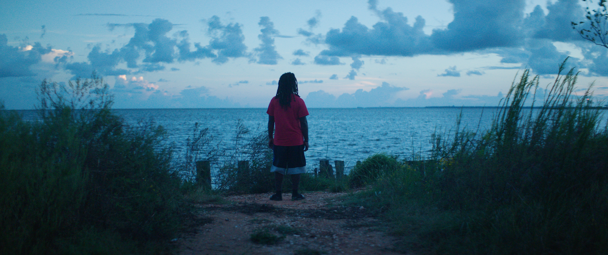 A Black man with dreads looks towards the ocean. From Margaret Brown’s ‘Descendant.’ Photo courtesy of Netflix. 