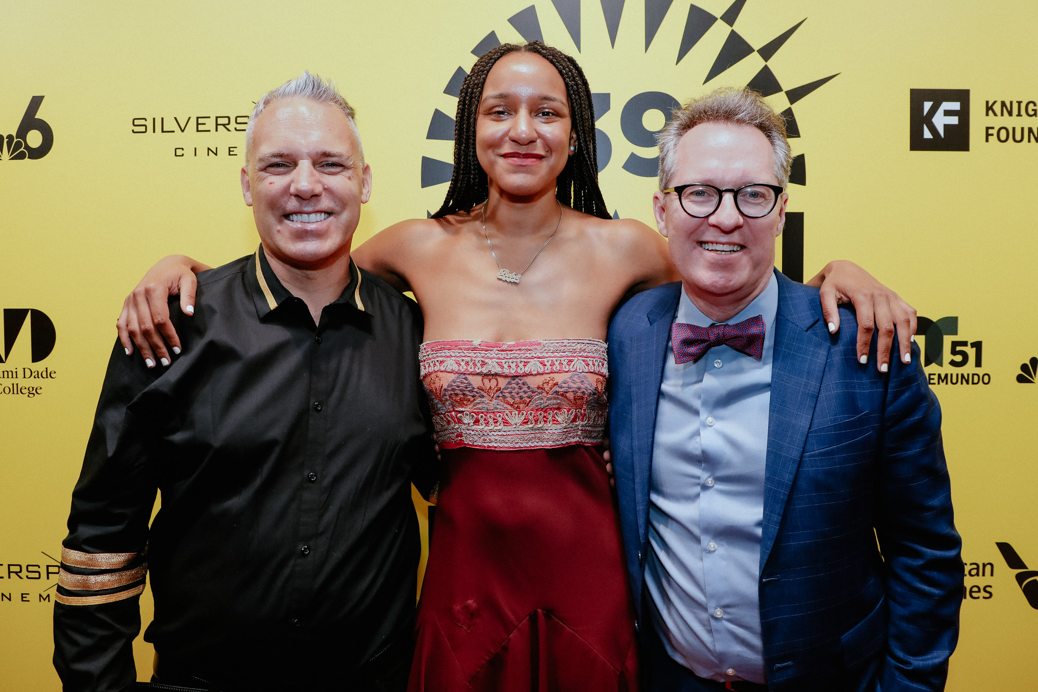 DOC NYC Artistic Director Jaie Laplante (left), a white man with white hair and a black shirt, and former DOC NYC Artistic Director Thom Powers, a white man with a blue shirt, blue blazer and red bowtie, flank Rebecca Huntt, an Afro-Latinx woman with braids and a patterned top, at the 2022 Miami Film Festival. Courtesy of Thom Powers.