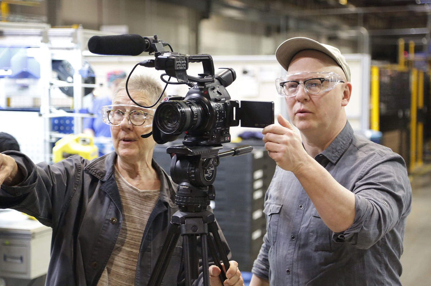 Julia Reichert (right), a white woman with short black hair, glasses and a black leather jacket, and Steven Bognar , a bald white man with glasses and a grey button-down shirt,, operating a camera,,in production on their 2018 film “American Factory.”  Courtesy of Netflix” 