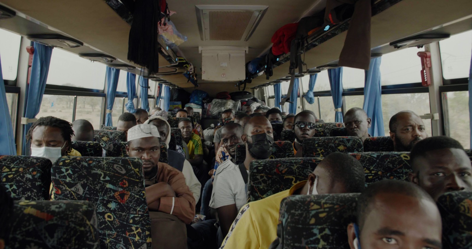 From the perspective of the front interior of a public transportation bus, a  group of African men are seated on a bus. From Ike Nnaebue's 'No U-Turn.' Courtesy of STEPS