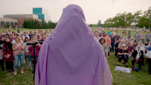 A woman wearing a lavender hijab stands on a podium looking out at a crowd. Photo: Capital-K Pictures. Courtesy of POV