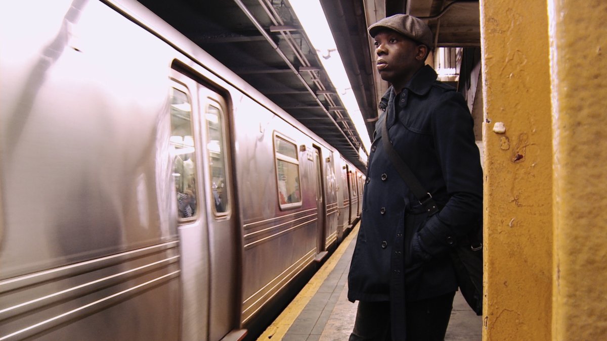 Marshall Ngwa, BeBe's conjurer, is a Black man hailing from Cameroon, waiting on a subway platform wearing a dark blue coat and brown cap. From Emily Branham’s ‘Being BeBe.’ Courtesy of the filmmaker.