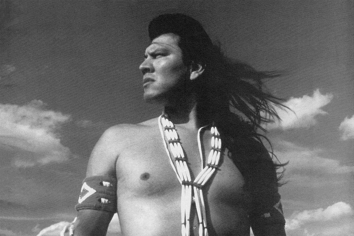 A Native American man, wearing traditional Indigenous accoutrements, stands in the middle of a plain, looking to his right. From the 1994 docuseries 'The Native Americans.' Courtesy of TBS