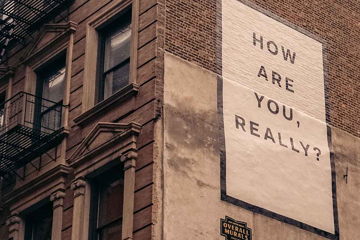 Stock image of a brownstone building with the words ‘How Are You, Really?’ painted on its side wall. Courtesy of Finn/Unsplash