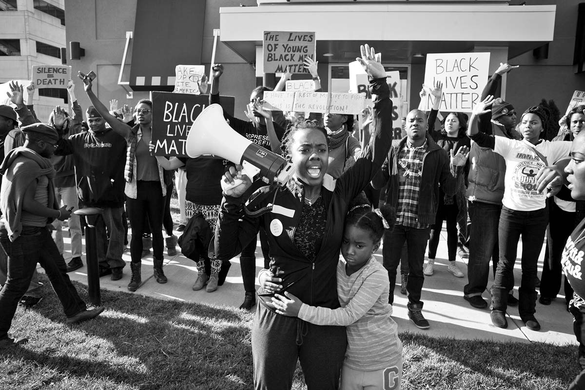 A Black woman with a megaphone raises her arm and shouts in a crowd of people. From Sabaah Folayan's  'Whose Streets?', a Magnolia Pictures release. Photo courtesy of Magnolia Pictures.