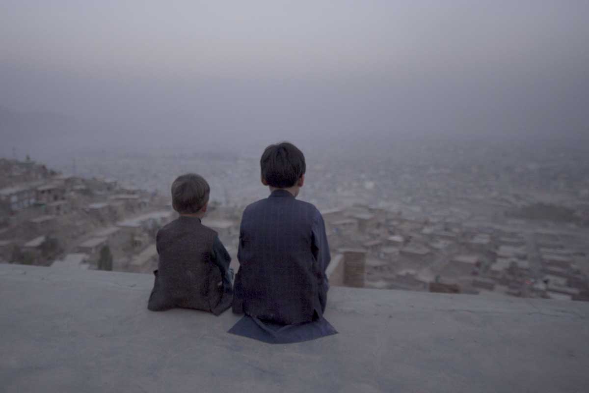 Young Afghani boys, Afshin and Benjamin, sit with their backs to the camera looking out at the city of Kabul. From Aboozar Amini’s ‘Kabul, City in the Wind.’ Courtesy of Movies that Matter.