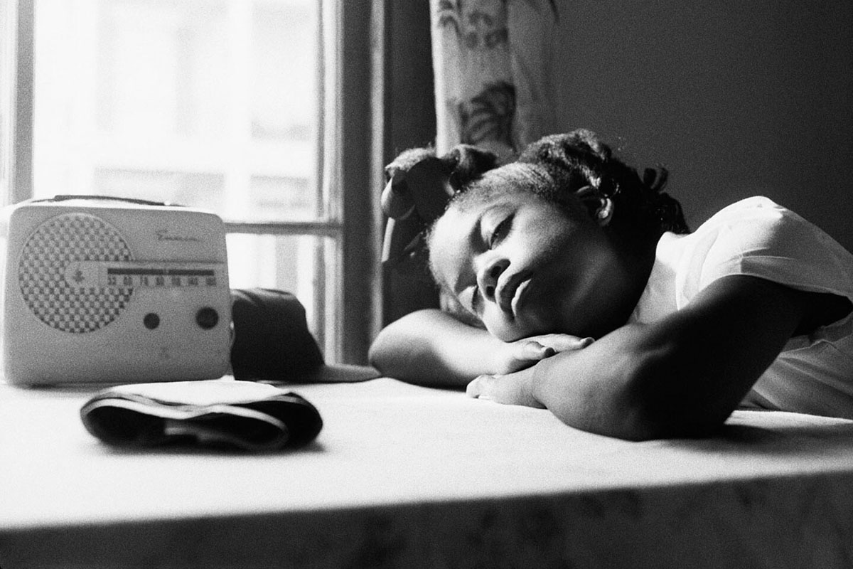 Black-and-white image of a young Black girl listening to the radio with her eyes closed. From Garrett Bradley’s ‘America.’ Courtesy of Museum of Modern Art
