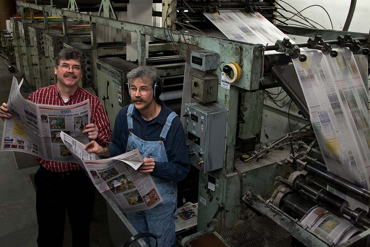 Brothers John and Art Cullen are two white men standing by a printing press, reviewing a hot-off-the-presses copy of 'The Storm Lake Times.' Image from Beth Levison and Jerry Risius’ ‘Storm Lake.’ Courtesy of 'Independent Lens'/PBS. 