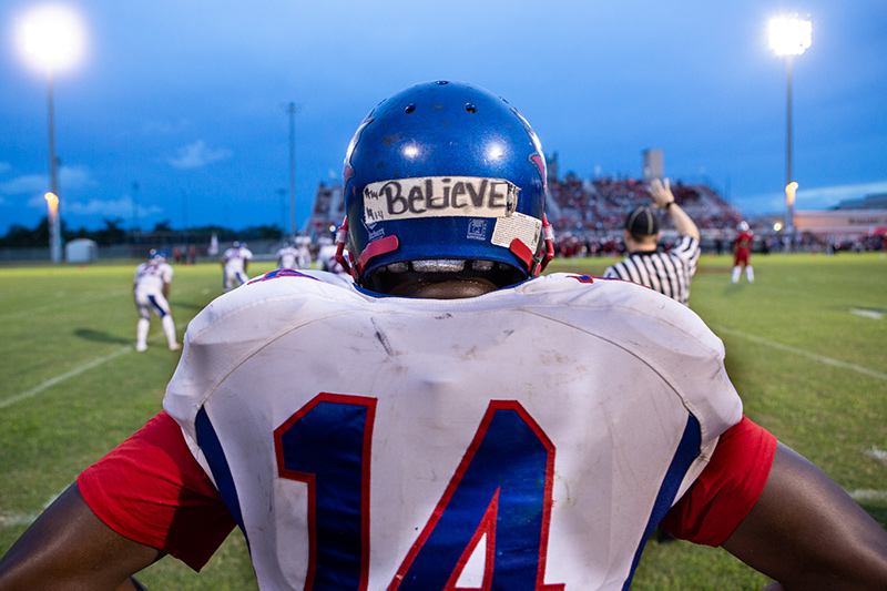 Back of a football player facing the field, his blue helmet has a horizontal tape with BELIEVE written with sharpie. From 'Pahokee,' directed by Ivete Lucas and Patrick Bresnan and produced by Maida Lynn. Courtesy of Visit Films