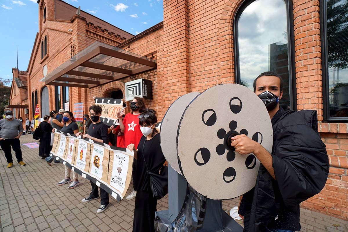 Cinemateca workers protest outside the Cinemateca Brasileira. They’re holding signs and cardboard cutouts of film reels. Photo by Benedito Faga / Alamy Stock Photo.