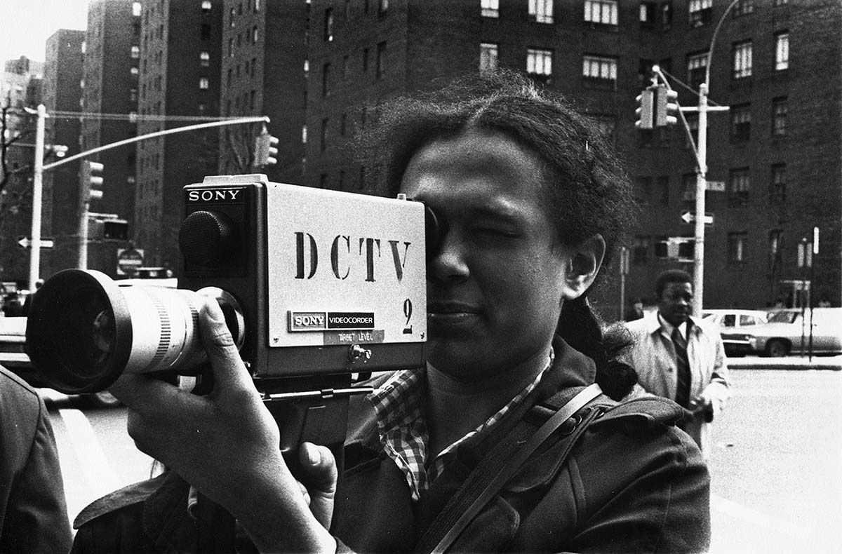 A black-and-white image of a woman with dark skin and dark curly hair holding an early Sony video camera. Courtesy of DCTV