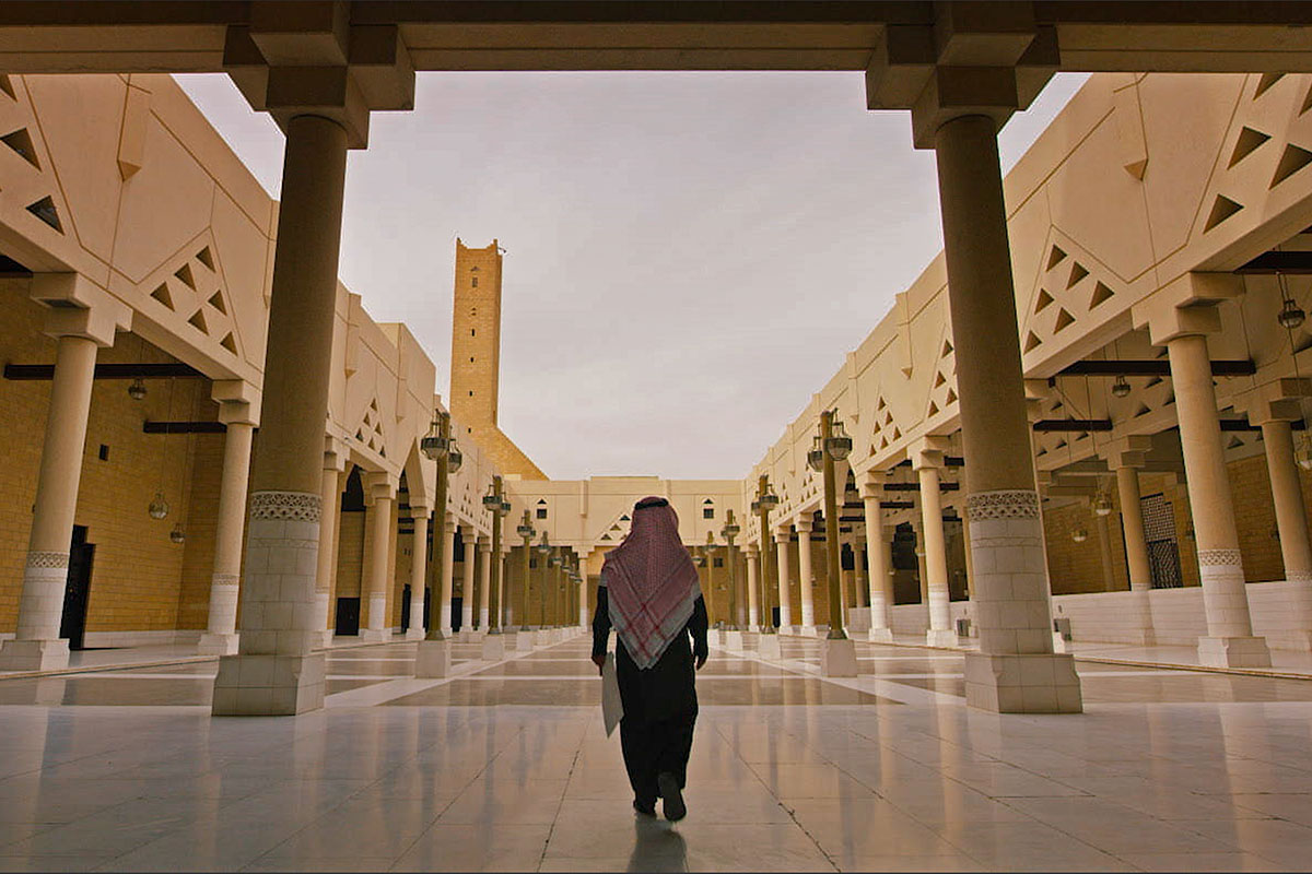 A Saudi Arabian man wearing a keffiyeh walks down a large, open courtyard of the Prince Mohammed Bin Nayef Centre for Counselling and Care. From Meg Smaker’s ‘Jihad Rehab.’ Courtesy of Sidestilt Films.