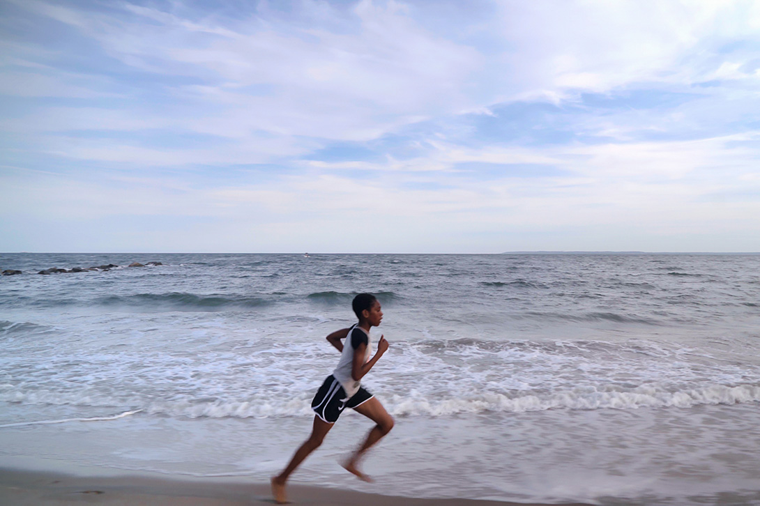  A young Black girl in shorts and a t-shirt runs along the seashore. Tai Sheppard in ‘Sisters on Track’ (directors: Corinne van der Borch, Tone Grøttjord-Glenne). Courtesy of Netflix