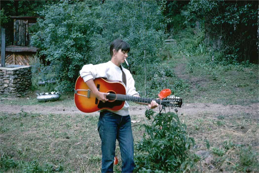 Karen Dalton is a white woman in a white sweater and blue jeans. She is playing a guitar and smoking a cigarette. Image from Richard Peete and Robert Yapkowitz’s ‘Karen Dalton: In My Own Time.’ Courtesy of The 2050 Group.