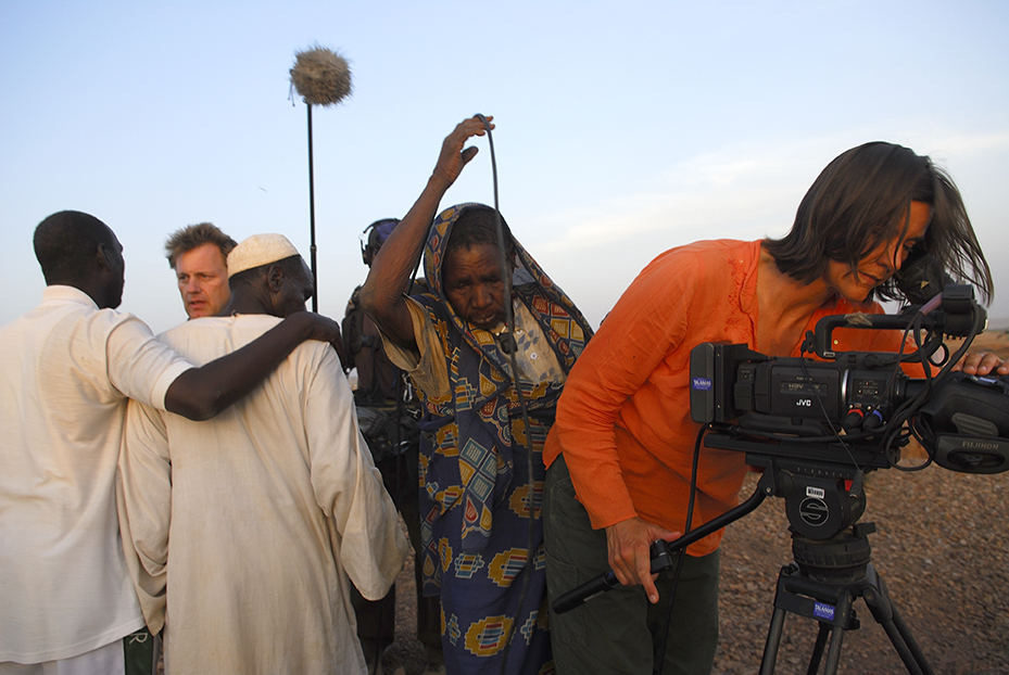 A camerawoman in orange long sleeve shooting in the dessert