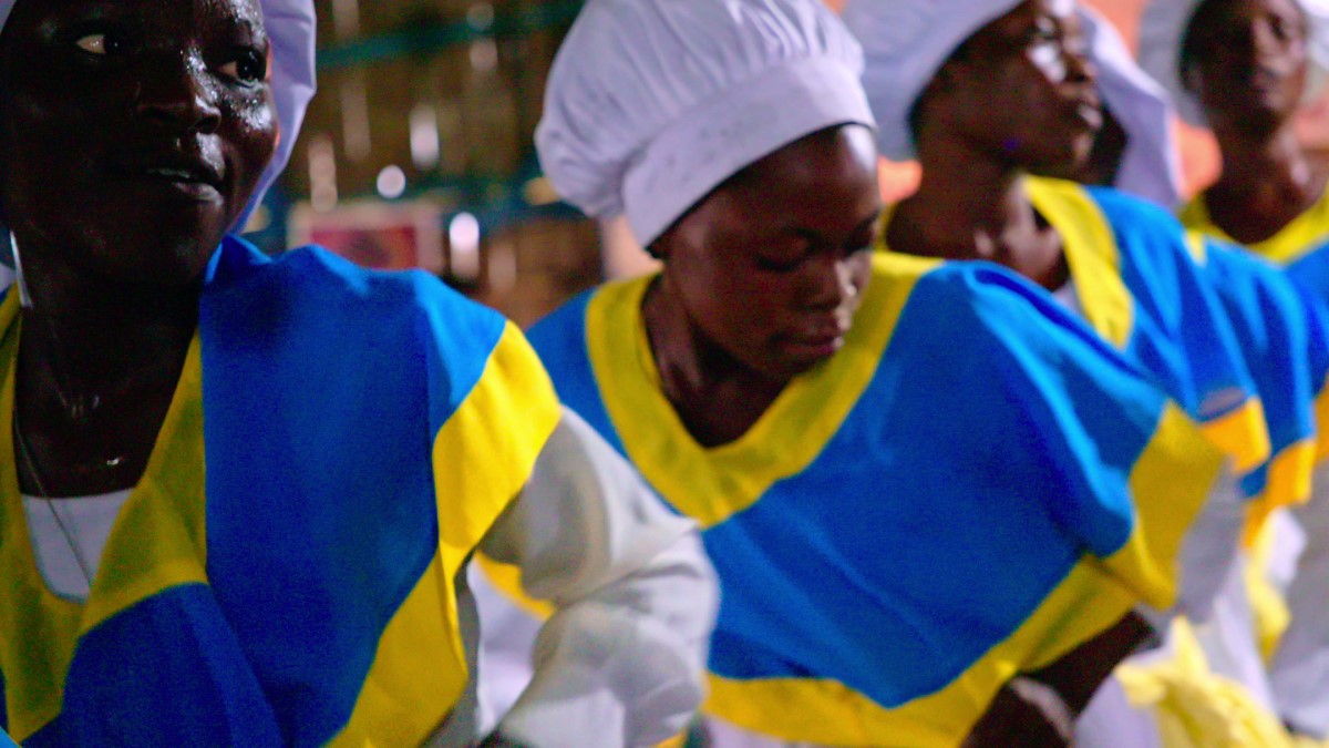 African women chefs in white hats and blue and yellow uniforms.