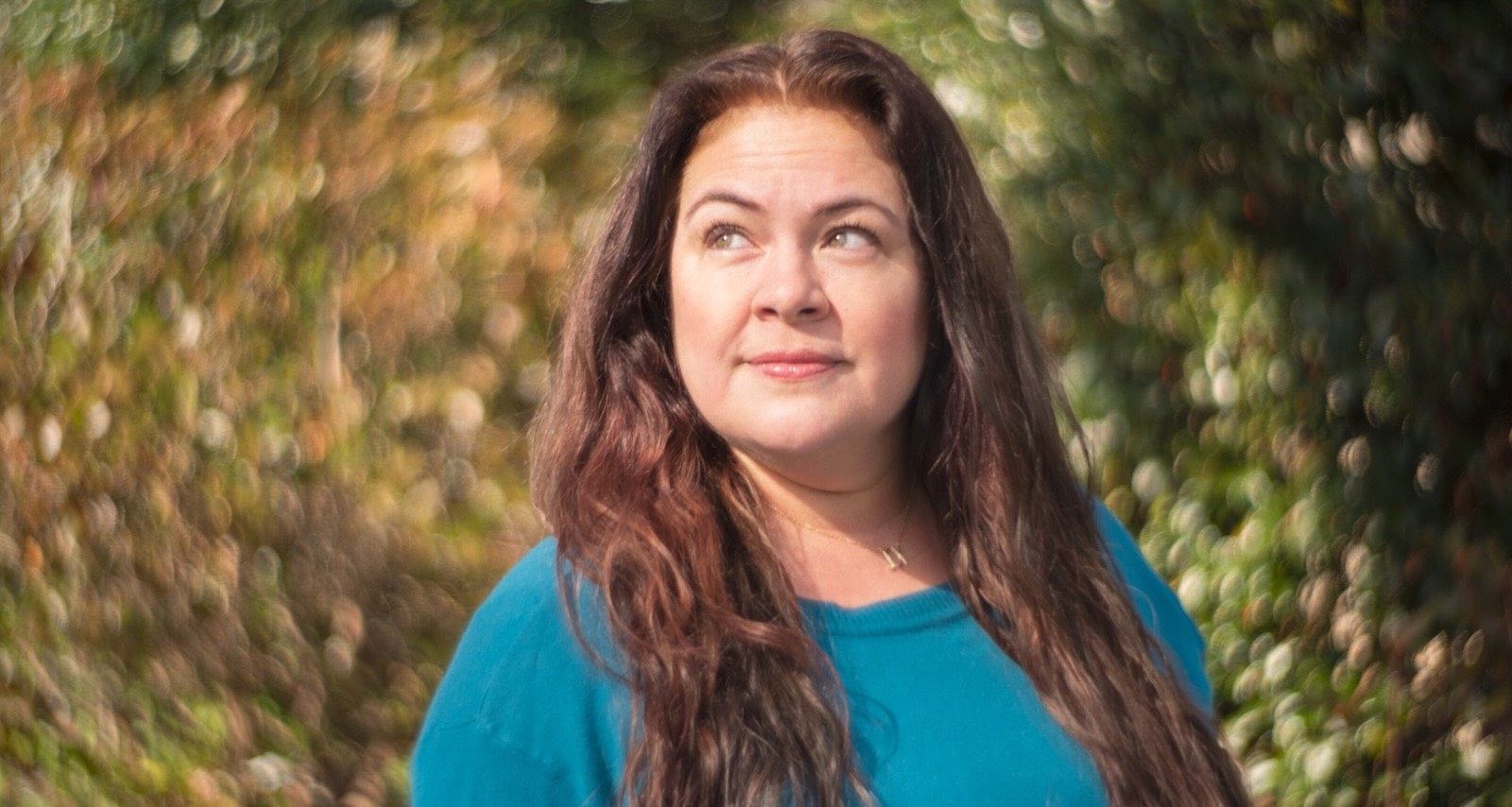 Headshot depicts Miroslava Gonzalez, a storyteller, community advocate, Producer, Writer and Director. She has long brown hair, green eyes and is wearing a teal-colored sweater.