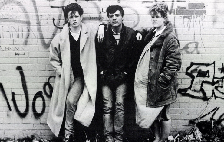 Three people wearing winter jackets pose in front of a brick wall sprayed with graffiti. From 'Living On The Edge', a documentary where Julian Petley examines the controversy surrounding the Broadcasting Bill. 