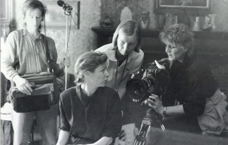 Four women in discussion about filmmaking; one holds a camera, another in the background holds a microphone. 