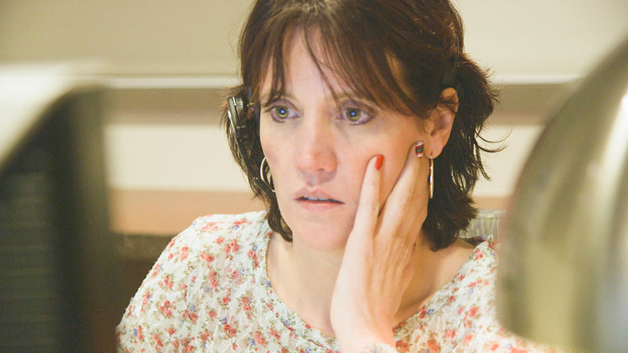 A white woman listening to a call through a headset, looking worried.