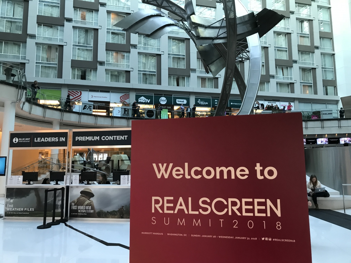A red sign with "Welcome to REALSCREEN SUMMIT 2018" in front of an open-air business lobby with abstract metal sculpture. Photo: Lauren Cardillo