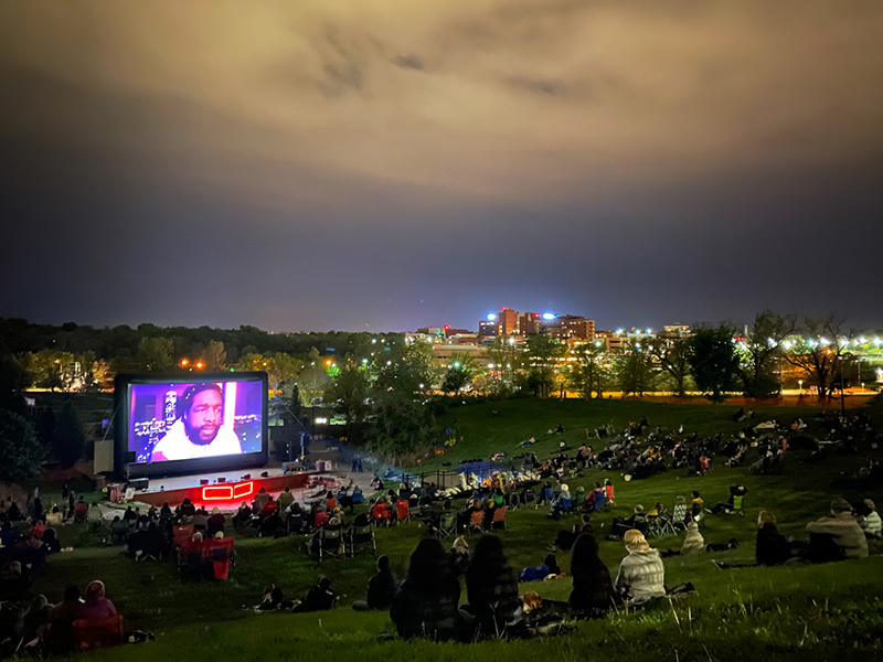 An outdoor nighttime screening: the audience sits on a grassy hill