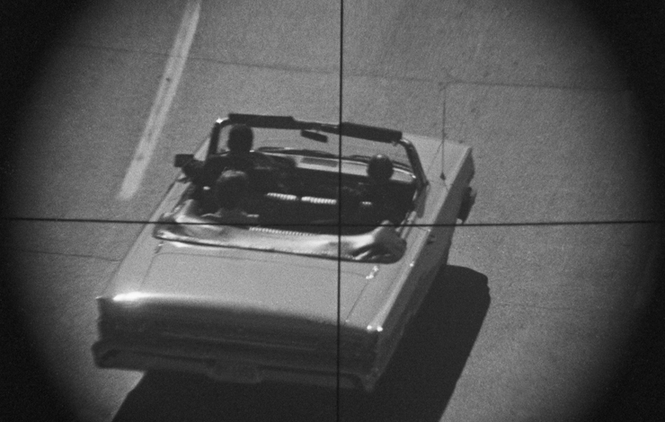 An overview of a car driving through the perspective of a telescopic site, from 'Who Shot President Kennedy.'