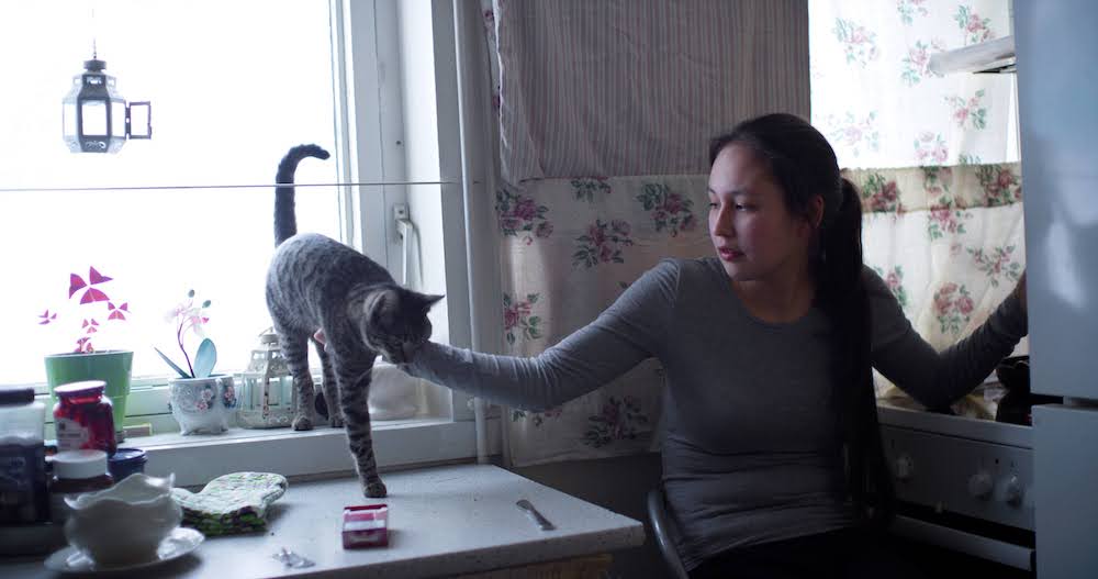 Kirsten Kleist Petersen is a young woman wearing a gray shirt. She is sitting on a chair by a window and petting her cat. From Sidse Torstholm Larsen and Sturla Pilskog’s ‘Winter’s Yearning.’ Courtesy of 'POV'.