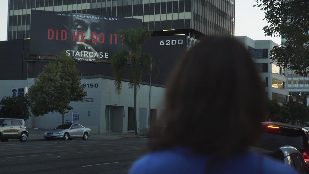 Margaret Ratliff is a white woman in a blue shirt. Her back faces the camera as she looks at a billboard advertising the TV series ‘The Staircase.’ From Jennifer Tiexiera and Camilla Hall’s ‘Subject.’ Photo courtesy of Susan Norget Film Promotion.  