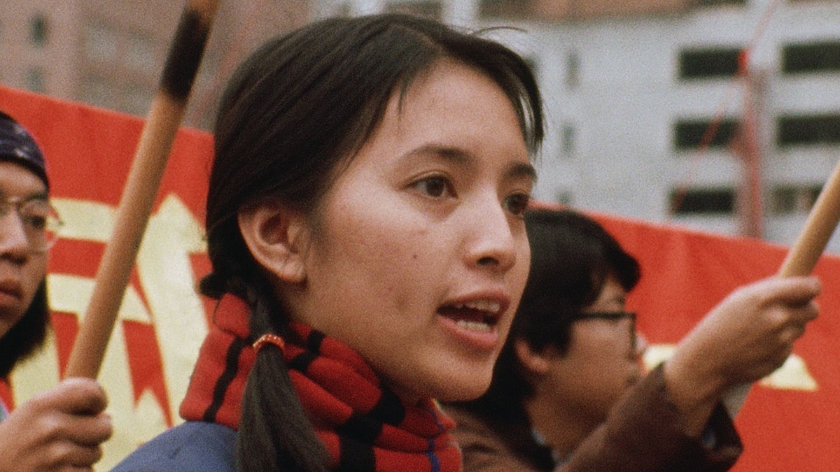 An Asian American woman, wearing shoulder-length pigtails, a red and black scarf and a blue shirt, participates in a protest march.  From ‘Chinatown Rising.’ Courtesy of ‘America Reframed’/World Channel