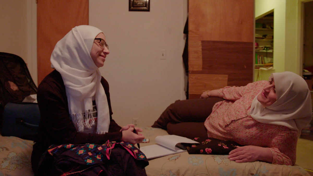 Two Muslim women wearing hijab smiling as they chat with one another. They are sitting on a bed. From Nausheen Dadabhoy's 'An Act of Worship.' Courtesy of Tribeca Festival.