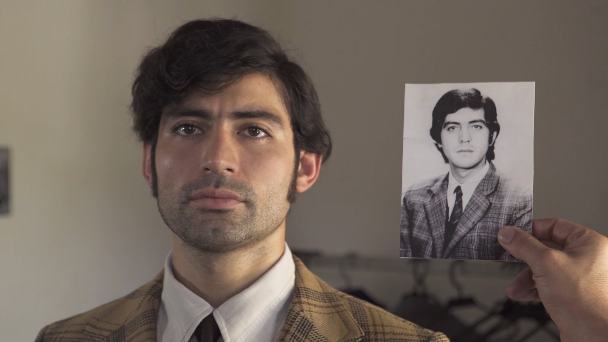 A Chilean male actor in a tan suit stands next to an old photograph of the Chilean male revolutionary he is playing. From Roberto Baeza's 'Meeting Point.' Courtesy of Hot Docs.