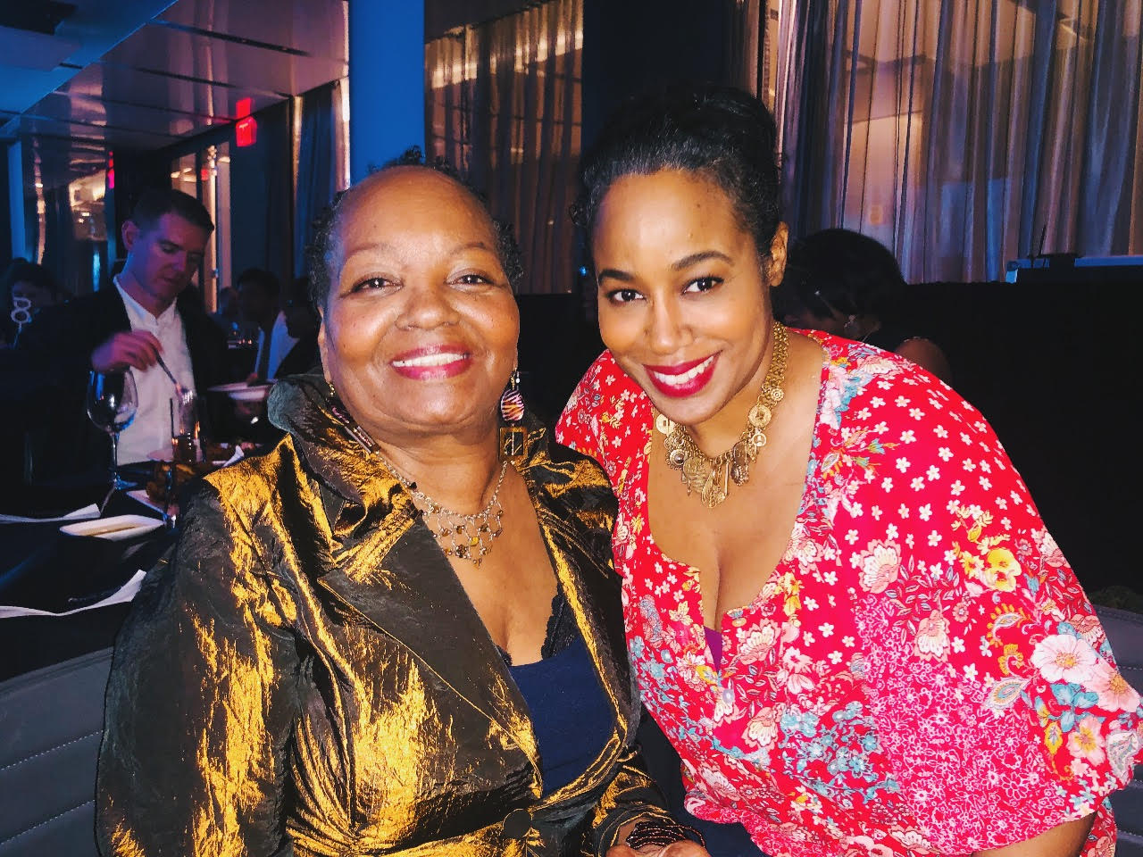 Filmmaker Sabrina Schmidt Gordon (right), a Black woman wearing a pint and red floral print shirt, with Mable Haddock, a Black woman wearing a gold jacket. Courtesy of Sabrina Schmidt Gordon.