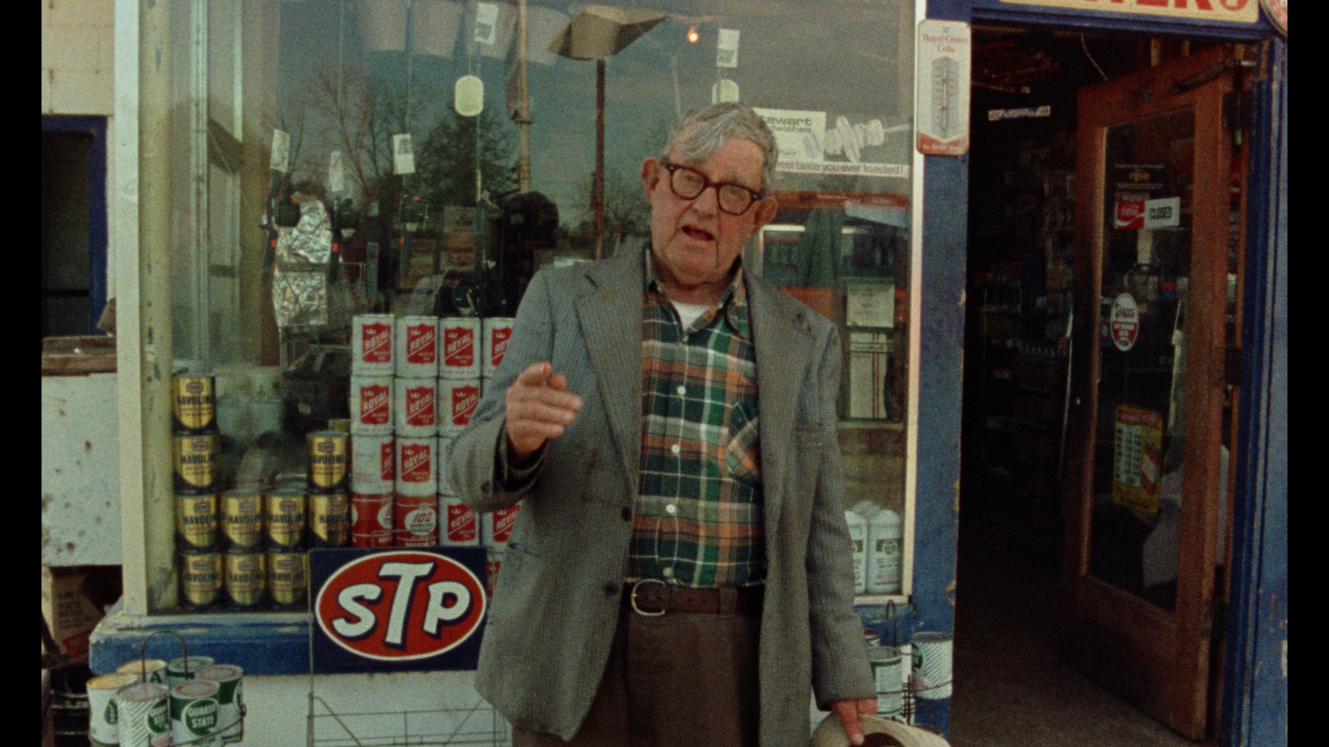 An older man with glasses and gray hair wearing a plaid shirt and blazer stands outside a storefront. He points at the camera while talking. From Errol Morris' Vernon, Florida.' Courtesy of Criterion Collection. 