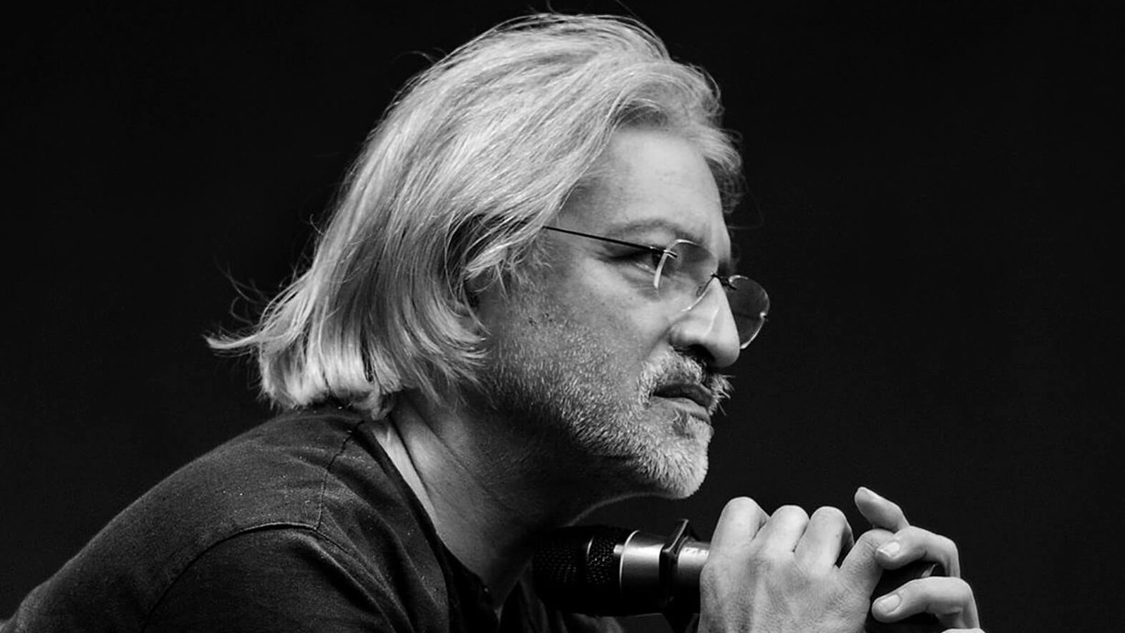 Photograph of Anand Patwardhan, a man with medium length silver hair, wearing glasses and holding a microphone.