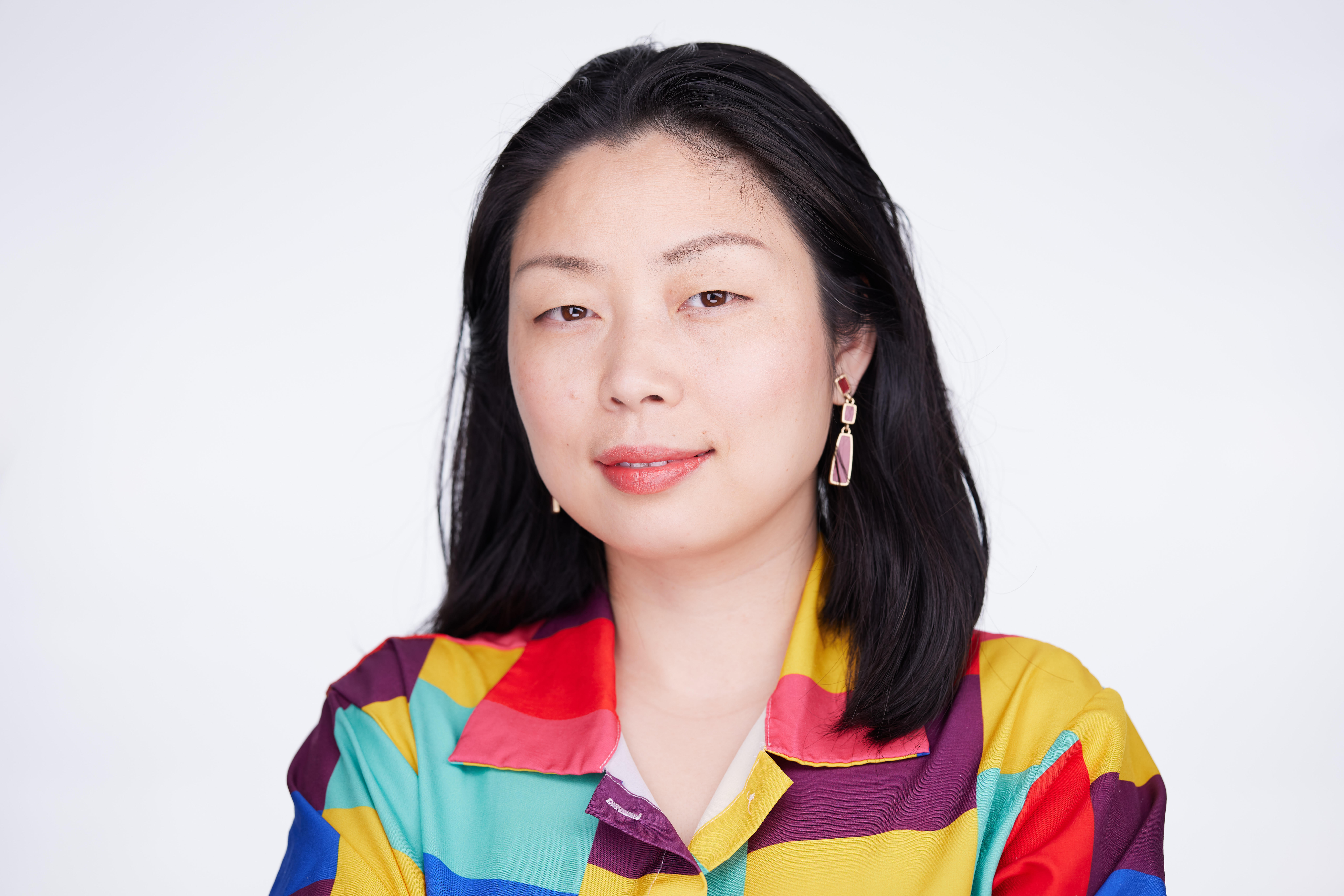 Photograph of Nanfu Wang, an Asian woman with black hair, wearing a colorful shirt and earrings, smiling.
