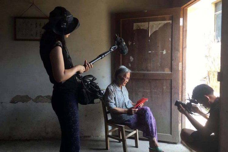 A cameraperson and boom operator record an older Asian woman with a red envelope in her hand. A behind the scenes shot from 'Hidden Letters' by Violet Du Feng. 