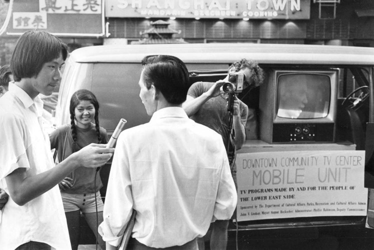 A black-and-white photo of a DCTV student conducting a man-on-the-street interview while another man, Jon Alpert, operates camera in front of their mobile unit. Courtesy of DCTV