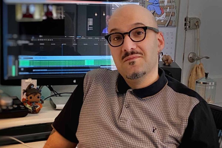 Editor Bo Mehrad, an Arab-American man, wearing glasses, a beige and black polo short, poses in front of his editing bay. Courtesy of Bo Mehrad.