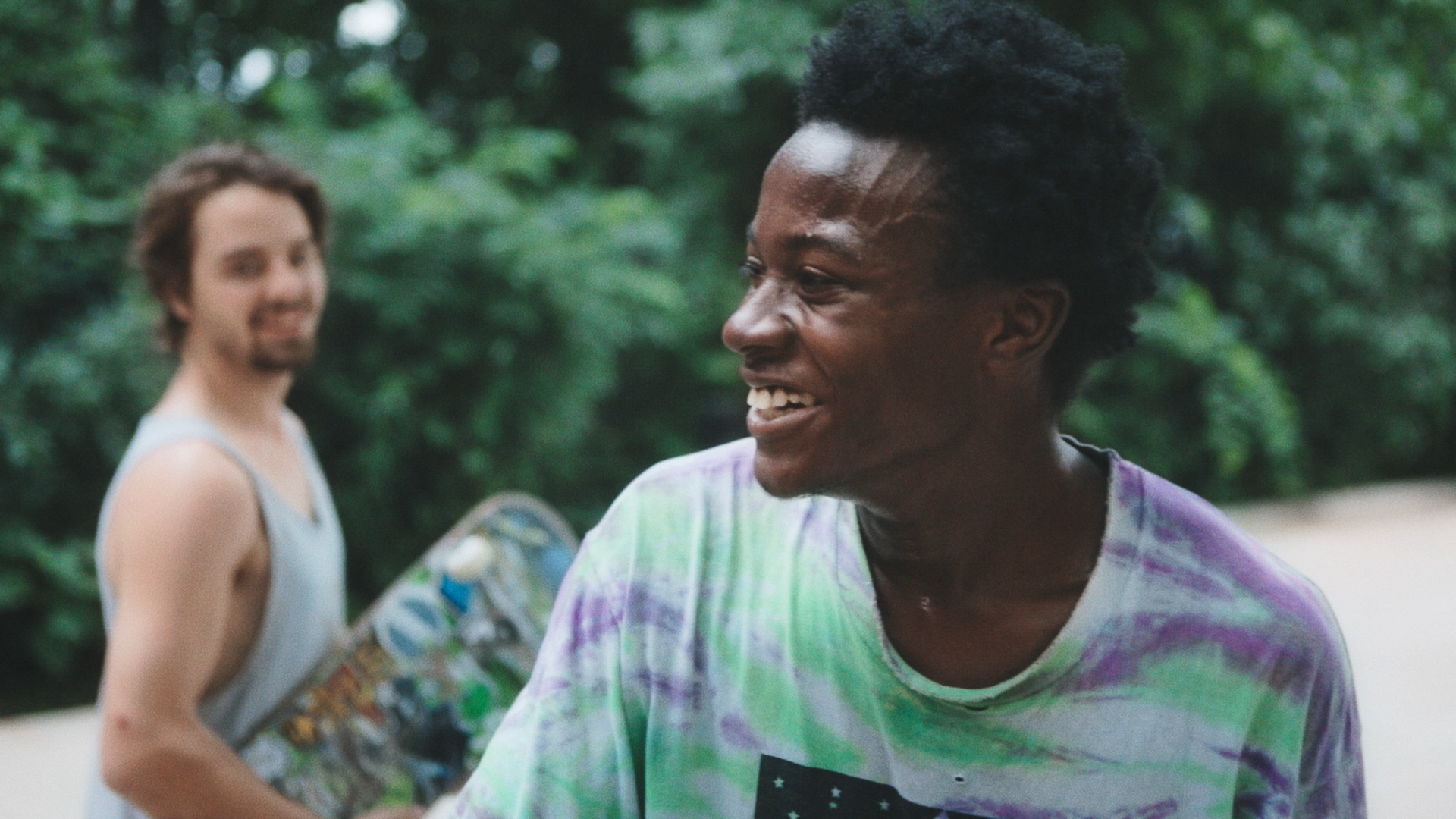 Two young men, one holding a skateboard, smile.